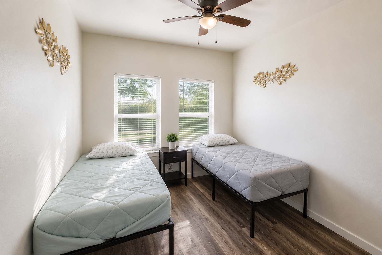 Shared bedroom with two twin beds, simple black frames, and leaf-shaped wall decor.