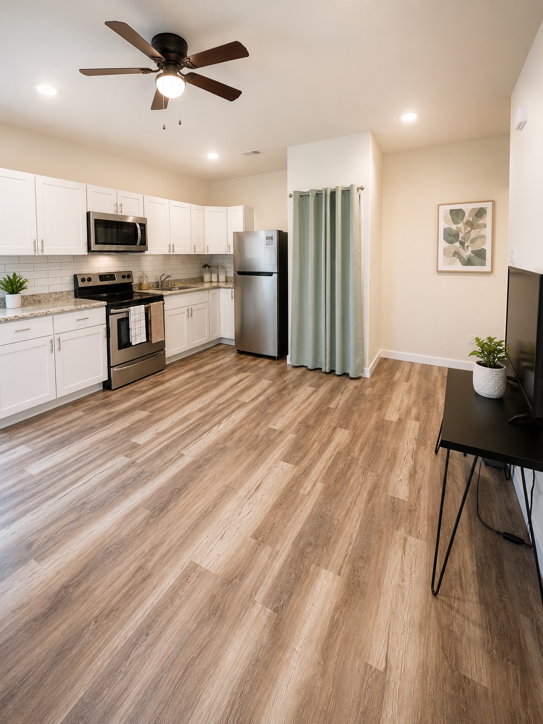 Open-concept kitchen with white cabinets, stainless steel appliances, and wood-look flooring.